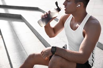 Man with fitness tracker drinking water after training outdoors, closeup