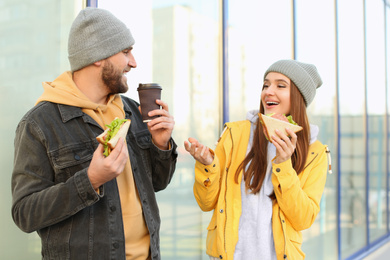 Photo of Happy young couple with sandwiches and coffee on city street