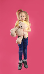 Little girl with teddy bear jumping on pink background