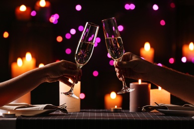 Young couple with glasses of champagne having romantic candlelight dinner at table, closeup
