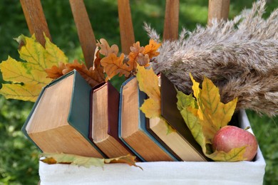 Different books, apple and maple leaves in wicker basket outdoors. Autumn atmosphere