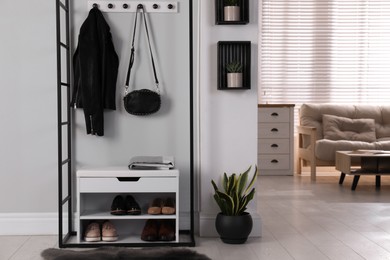 Stylish storage cabinet with different pairs of shoes near white wall in hall
