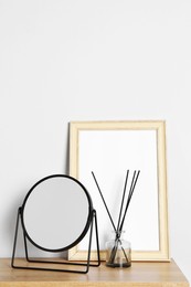 Photo of Stylish mirror, reed diffuser and picture frame on table near light wall