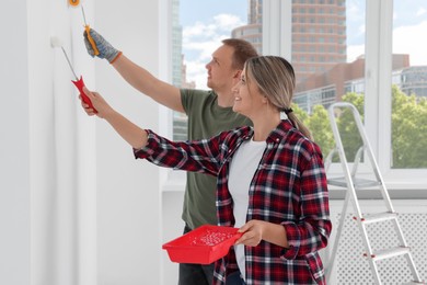 Happy couple painting wall in apartment during repair