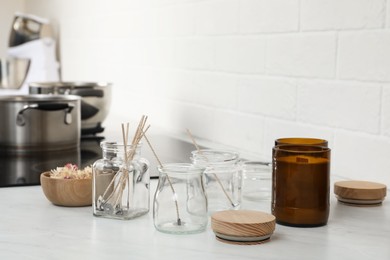 Glass jars with wicks and dry flowers near homemade candles on kitchen counter
