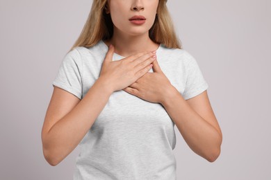 Young woman suffering from pain during breathing on light grey background, closeup