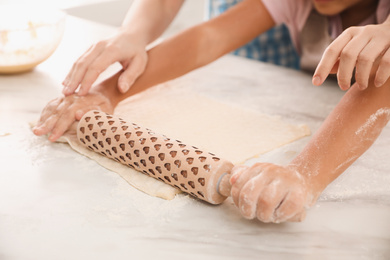 Mother and daughter rolling dough together at table, closeup
