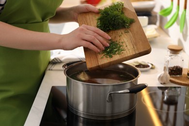Woman putting dill into pot to make bouillon in kitchen, closeup. Homemade recipe