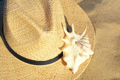 Stylish straw hat and sea shell on sandy beach, closeup