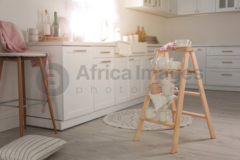 Photo of Decorative ladder with different dishware and field flowers bouquet in stylish kitchen. Idea for interior design