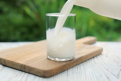 Pouring tasty fresh milk into glass on white wooden table, closeup