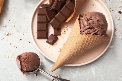 Delicious ice cream in wafer cone and chocolate pieces on light grey table, flat lay