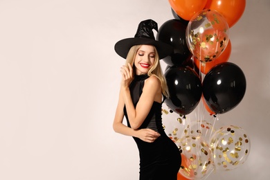 Beautiful woman in witch costume with balloons on white background, space for text. Halloween party