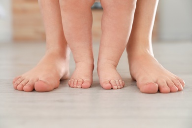Mother and her baby standing on floor, closeup of legs