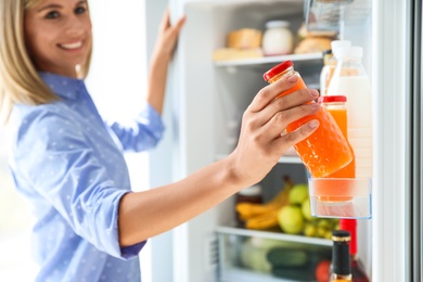 Woman taking bottle with juice out of refrigerator in kitchen