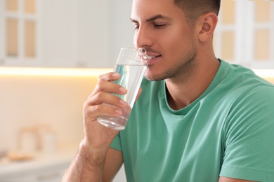 Man drinking pure water from glass in kitchen, closeup