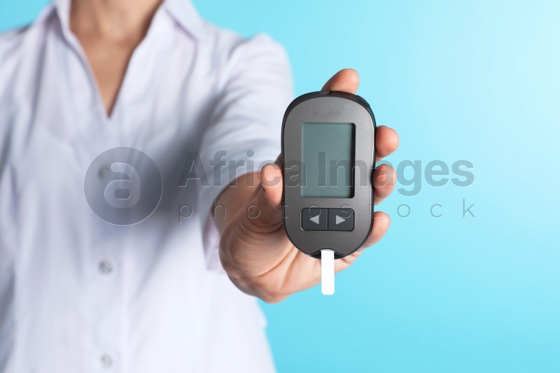 Female doctor holding digital glucometer on color background, closeup. Medical object