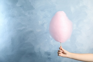 Woman holding sweet pink cotton candy on light blue background, closeup view. Space for text