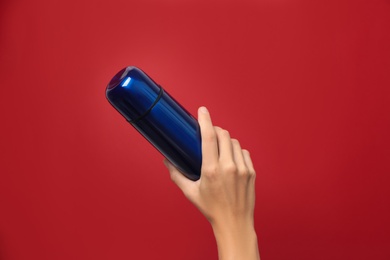 Woman holding modern blue thermos on red background, closeup