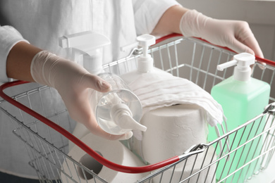 Woman with shopping basket full of antiseptics and toilet paper, closeup. Panic caused by virus