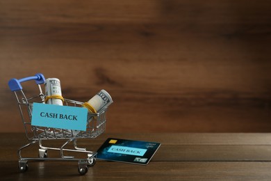 Credit card and small shopping cart with signs Cash Back on wooden table. Space for text