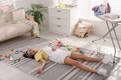 Tired young mother sleeping on floor in messy living room