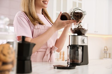 Woman using electric coffee grinder in kitchen, closeup