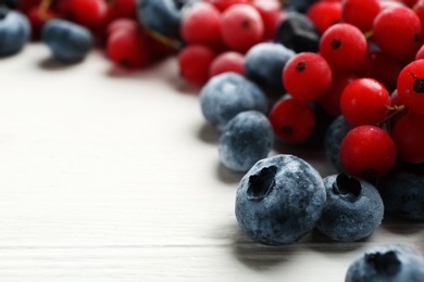 Tasty frozen blueberries and red currants on white wooden table, closeup. Space for text