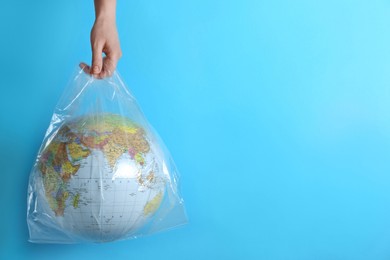 Photo of Woman holding plastic bag with globe and space for text on turquoise background, closeup. Environmental conservation