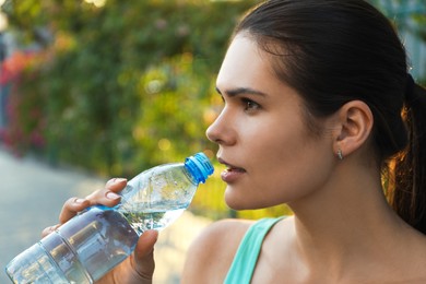 Photo of Young woman drinking water outdoors on hot summer day. Refreshing drink