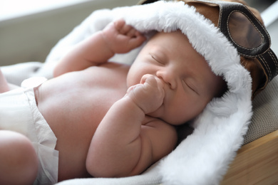 Cute newborn baby in aviator hat sleeping on blanket, closeup