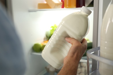 Man with gallon of milk near refrigerator indoors, closeup