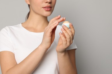 Young woman with lip balm on grey background, closeup