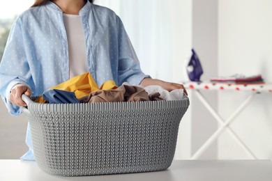 Woman with basket full of clean laundry at table indoors, closeup