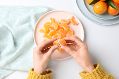 Woman holding fresh juicy tangerine at white table, top view