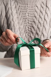 Photo of Woman decorating gift box at white table, closeup. Christmas present