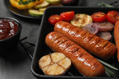 Delicious grilled sausages and vegetables on grey table, closeup