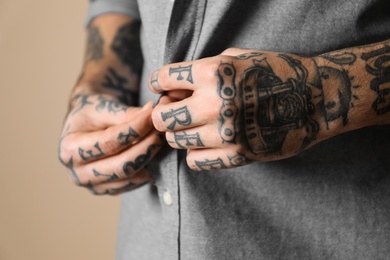 Photo of Young man with tattoos on body against beige background, closeup