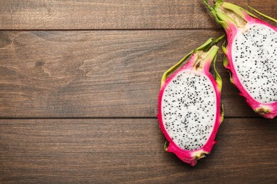 Halves of delicious dragon fruit (pitahaya) on wooden table, flat lay. Space for text