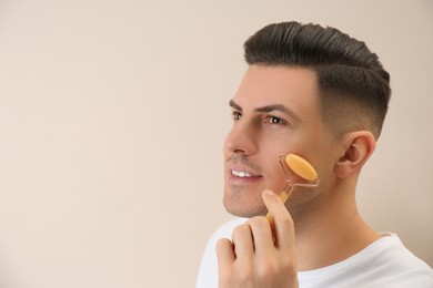 Man using mineral facial roller on beige background. Space for text