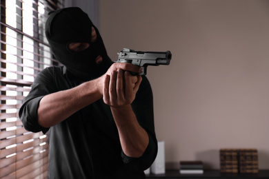 Man in mask holding gun indoors, focus on hands