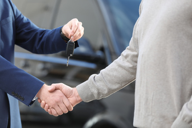 Salesman giving key to customer while shaking hands in modern auto dealership, closeup. Buying new car