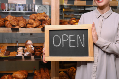 Female business owner holding OPEN sign in bakery, closeup