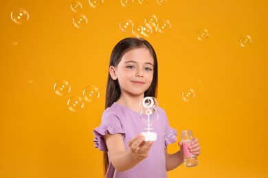Little girl having fun with soap bubbles on yellow background