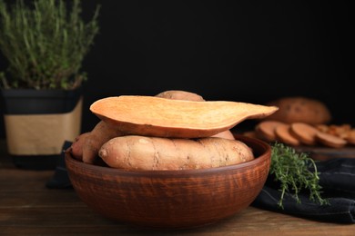 Cut and whole sweet potatoes in bowl on wooden table