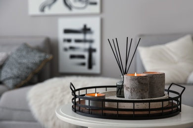 Candles and aroma reed diffuser on white table near grey sofa, space for text