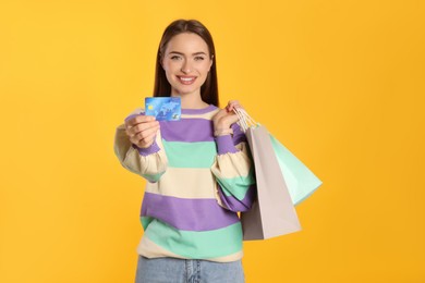 Photo of Happy young woman holding shopping bags against yellow background, focus on hand with credit card. Big sale