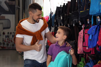 Little school boy with father choosing backpack in supermarket