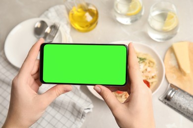 Image of Chroma key compositing. Woman holding smartphone with green screen at table indoors, closeup. Mockup for design