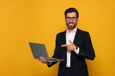 Smiling bearded man pointing at laptop on orange background
